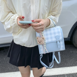 Detail of light blue gingham mini backpack with cute teddy bear charm on a model