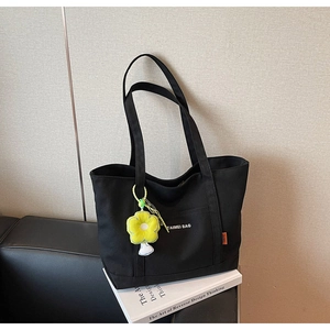Dettaglio borsa shopper in tela nera con scritte bianche e ciondolo a forma di girasole