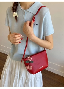 Red leather underarm bag with a cherry charm and white logo on a lifestyle model