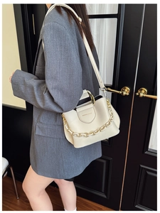 Detail view of cream white bucket bag with gold chain strap on a model wearing grey blazer