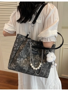 Floral print tote bag with pearl chain and plush charm shown on model in a modern room