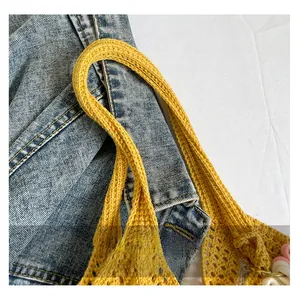 Close-up of yellow woven shoulder bag with floral charm on blue denim background