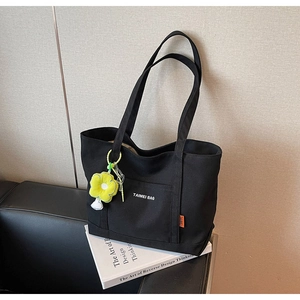 Dettaglio della borsa tote in tela nera con ciondolo a fiore giallo su un divano