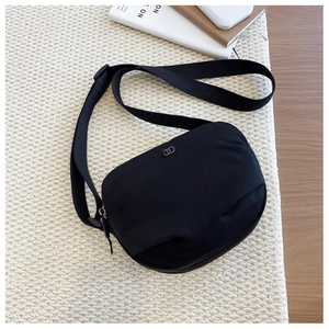 Detail view of black nylon shoulder bag featuring wide fabric strap and metal logo