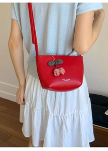 Detail of red leather bucket bag featuring a cherry charm and white brand logo printing