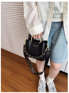 Detail of black leather bucket bag with gold circular handle and patterned wide strap