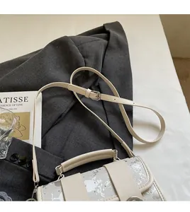 Détail du sac oreiller crème à texture argentée sur un blazer gris avec un magazine