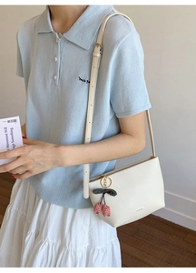 Chic cream tote bag with cherry charm detail shown with a blue knit outfit