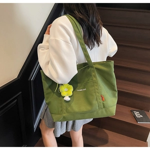 Dettaglio di borsa tote in tela verde con ciondolo a fiore e logo sulle scale