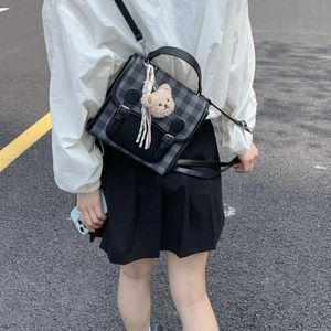 Detail of grey plaid flap crossbody bag with plush bear charm and ribbon accent