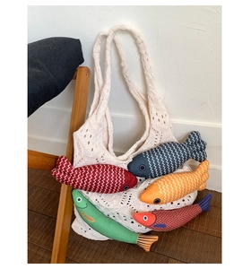 Detail of colorful fish plush toys inside a knitted tote bag on a wooden chair