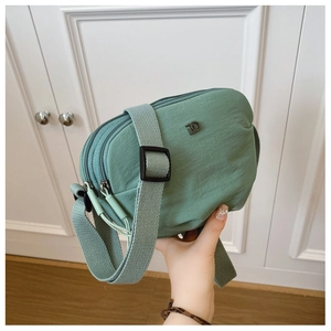 Detail view of mint green nylon crossbody bag with three zipper compartments and wide strap