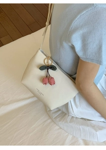 Detail der cremefarbenen Tragetasche mit rotem Kirschanhänger und aufgedrucktem Logo