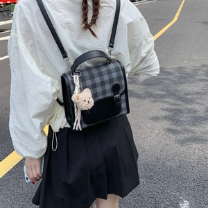 Detail of grey plaid backpack with leather buckle and cute beige teddy bear charm accessory