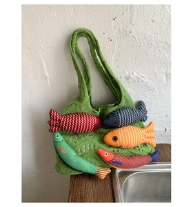 Close-up of green knit tote bag with colorful stuffed fish charms and crochet details