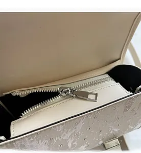 Détail de la fermeture éclair en métal argenté sur un sac beige orné de petits clous