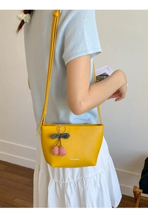 Detail of yellow leather crossbody bag with cherry charm accessory and brand logo