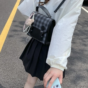 Detail of grey plaid crossbody bag with a cute bear keychain and black strap accents