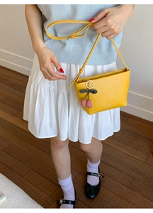 Detail of yellow leather tote bag with cherry charm worn by a model in a casual outfit