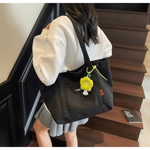 Dettaglio della borsa tote in tela nera con ciondolo a fiore portata a spalla sulle scale