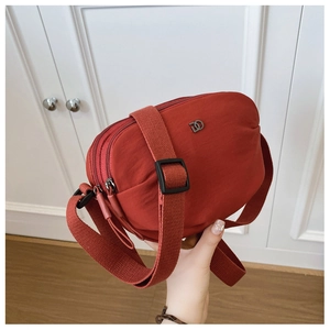 Detail view of the brick red nylon crossbody bag with dual zippers and DD metal logo