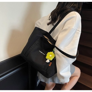 Dettaglio della borsa tote in tela nera con etichetta arancione e ciondolo a fiore