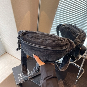 Detail of black washed denim chest bag featuring woven zipper pull and adjustable strap