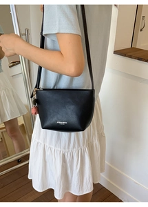 Detail view of black leather crossbody bucket bag with strawberry charm and white logo text