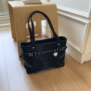 Detail of black glossy tote bag with metal buckle straps and silver heart pendant