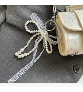 Détail d'un charme nœud en perles avec ruban en dentelle sur un sac à main blanc cassé
