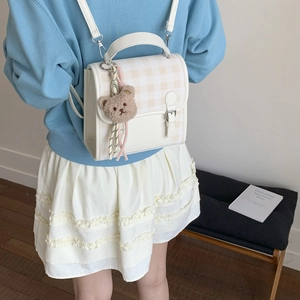 Detail of a chic cream patchwork mini backpack with a teddy bear charm and plaid pattern