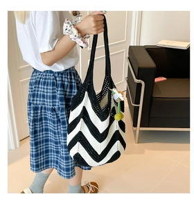 Close-up of black and white chevron knit tote bag with a green floral charm accessory