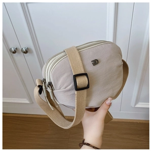 Detail view of the beige nylon crossbody bag featuring three zippered compartments and metal logo