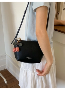 Detail of black leather bucket bag featuring a cherry charm and white brand logo