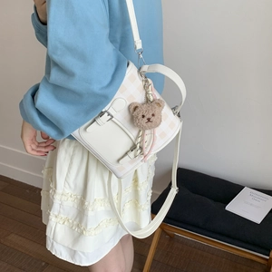 Close-up of white plaid PU leather crossbody bag with cute brown teddy bear pendant detail