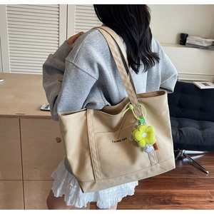 Dettaglio di una borsa tote in tela beige con ciondolo floreale e logo su modella