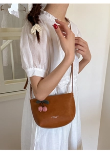 Detail of brown half-moon crossbody bag with cherry charm worn with white dress