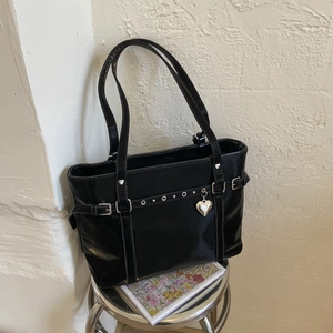Close-up of black Y2K tote bag with silver eyelets and heart charm on a metal stool