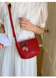 Detail der roten Lederbeuteltasche mit Kirschanhänger und weißem Logo auf weißem Kleid