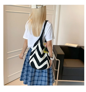 Detail of hand-woven knit tote bag with black and white V-pattern and daisy charm