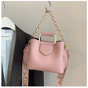 Detail of pink bucket bag with wavy edges, gold handle, and embroidered strap