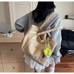 Dettaglio della borsa tote in tela crema con ciondolo a fiore e logo stampato