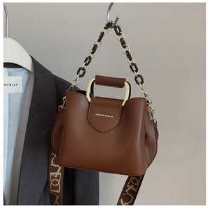 Detail of a brown leather bucket bag featuring a gold metal handle and wide fabric strap