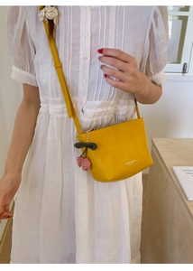 Detail der gelben Leder-Eimertasche mit rotem Kirschanhänger und Markenlogo-Akzent
