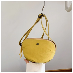 Close-up of mustard yellow nylon crossbody bag with metal D-logo and adjustable strap