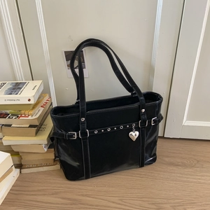 Detail of glossy black tote bag with silver eyelets and a heart-shaped metal pendant charm
