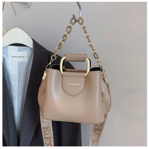 Detail of beige bucket bag featuring amber acrylic chain and woven patterned strap