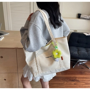 Dettaglio della borsa tote in tela bianco avorio con ciondolo a fiore di peluche giallo