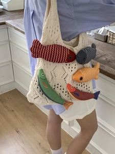 Knitted hollow tote bag with colorful 3D fish charms shown in a home setting