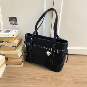 Detail of black faux leather tote with heart pendant and silver rivets on wood floor